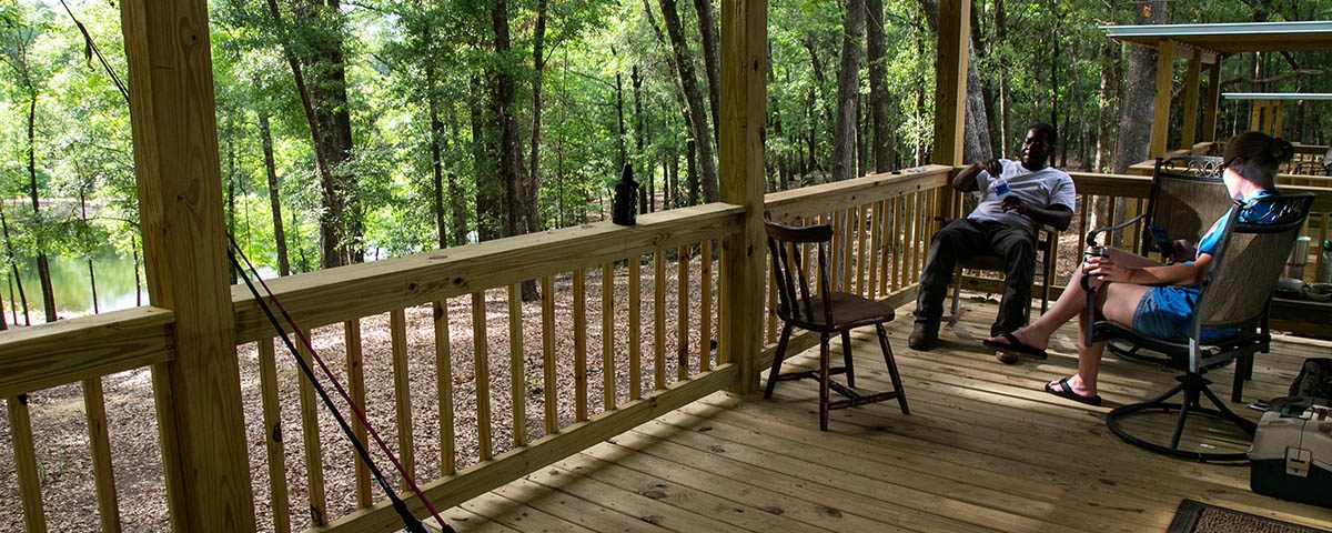 Guests relaxing on a wooded porch near the water during spring at The Oaks RV Park in Andalusia, Alabama