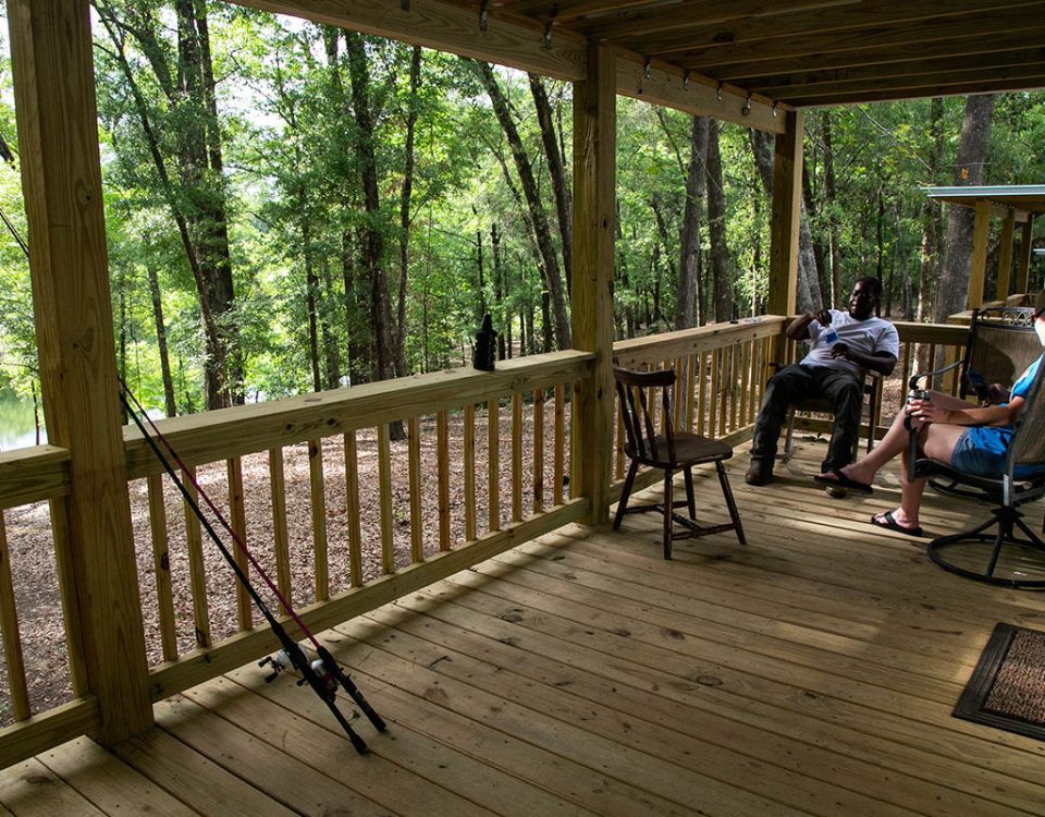 Guests relaxing on a wooded porch near the water during spring at The Oaks RV Park in Andalusia, Alabama