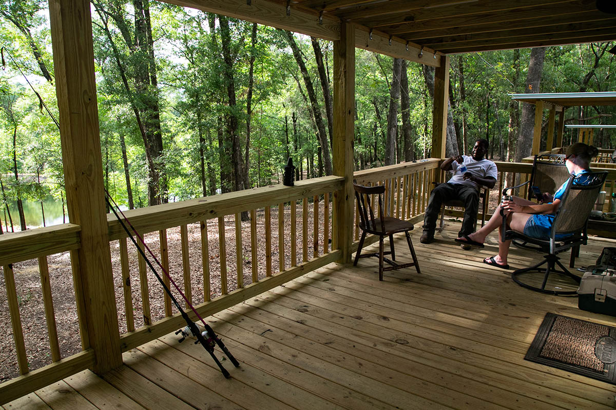 Guests relaxing on a wooded porch near the water during spring at The Oaks RV Park in Andalusia, Alabama